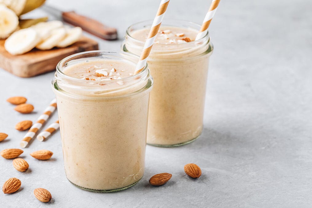 Banana almond smoothie with cinnamon and oat flakes and coconut milk in glass jars