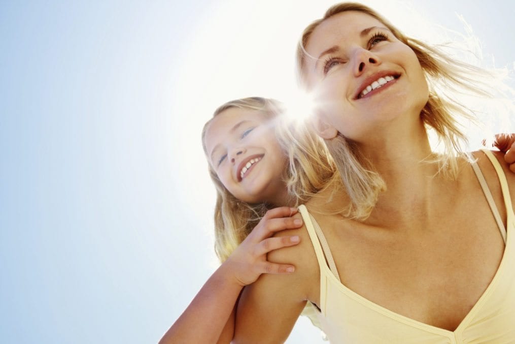 Cute little girl being piggybacked by mother on a bright sunny day